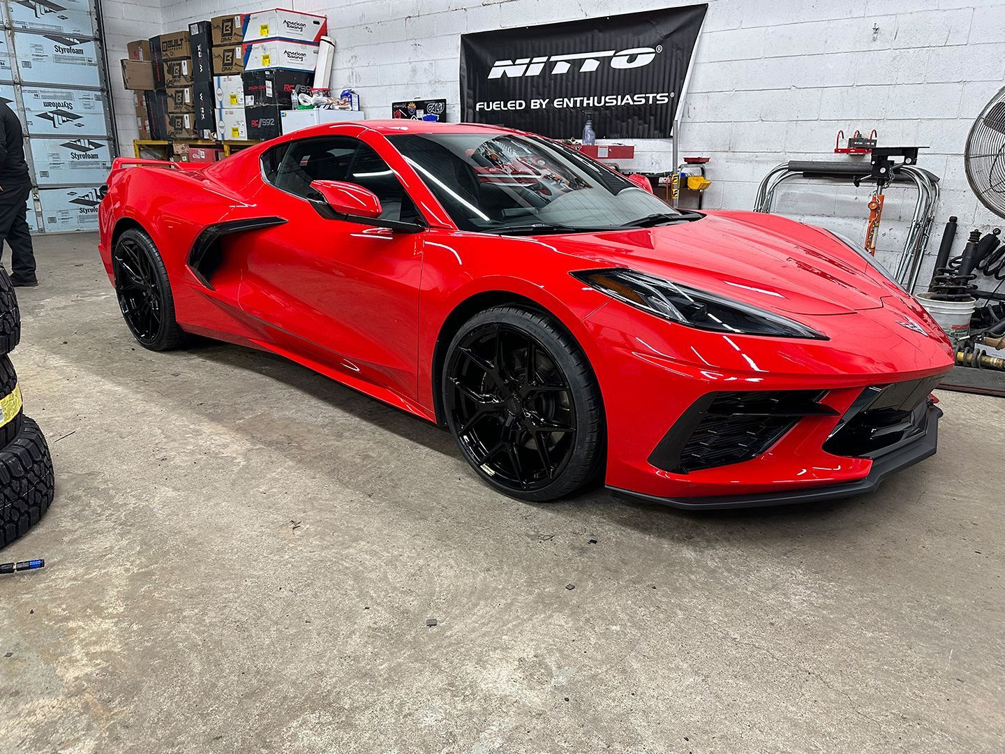 A red sports car is parked in a garage next to a tire.