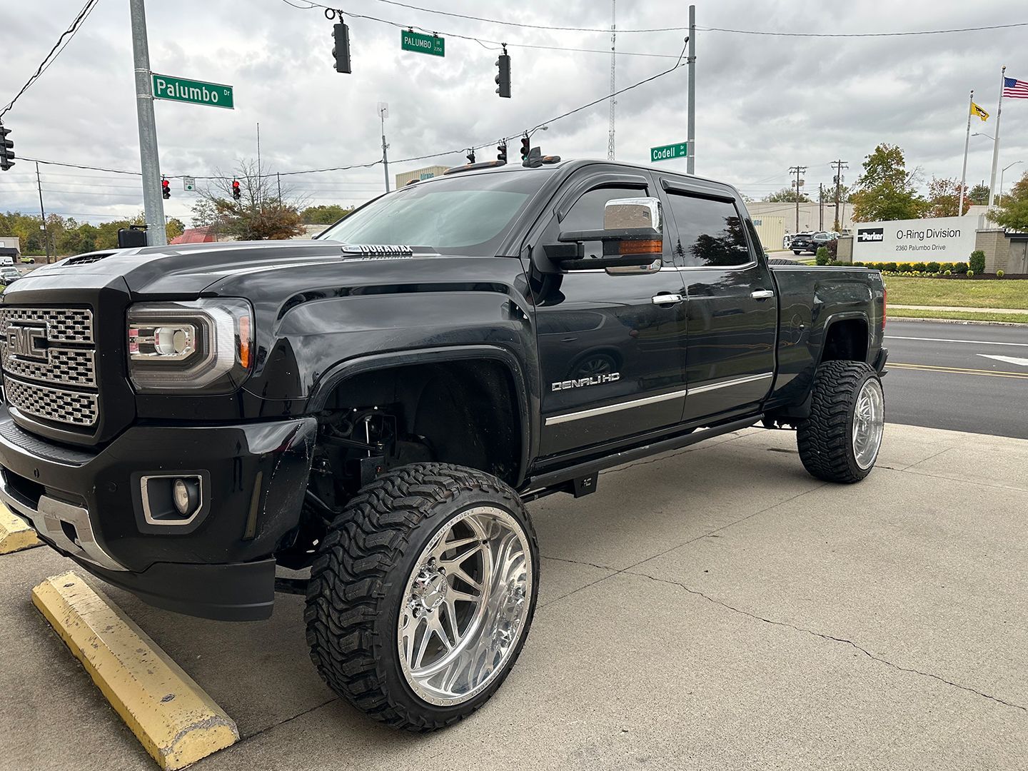 A black truck is parked on the side of the road in a parking lot.