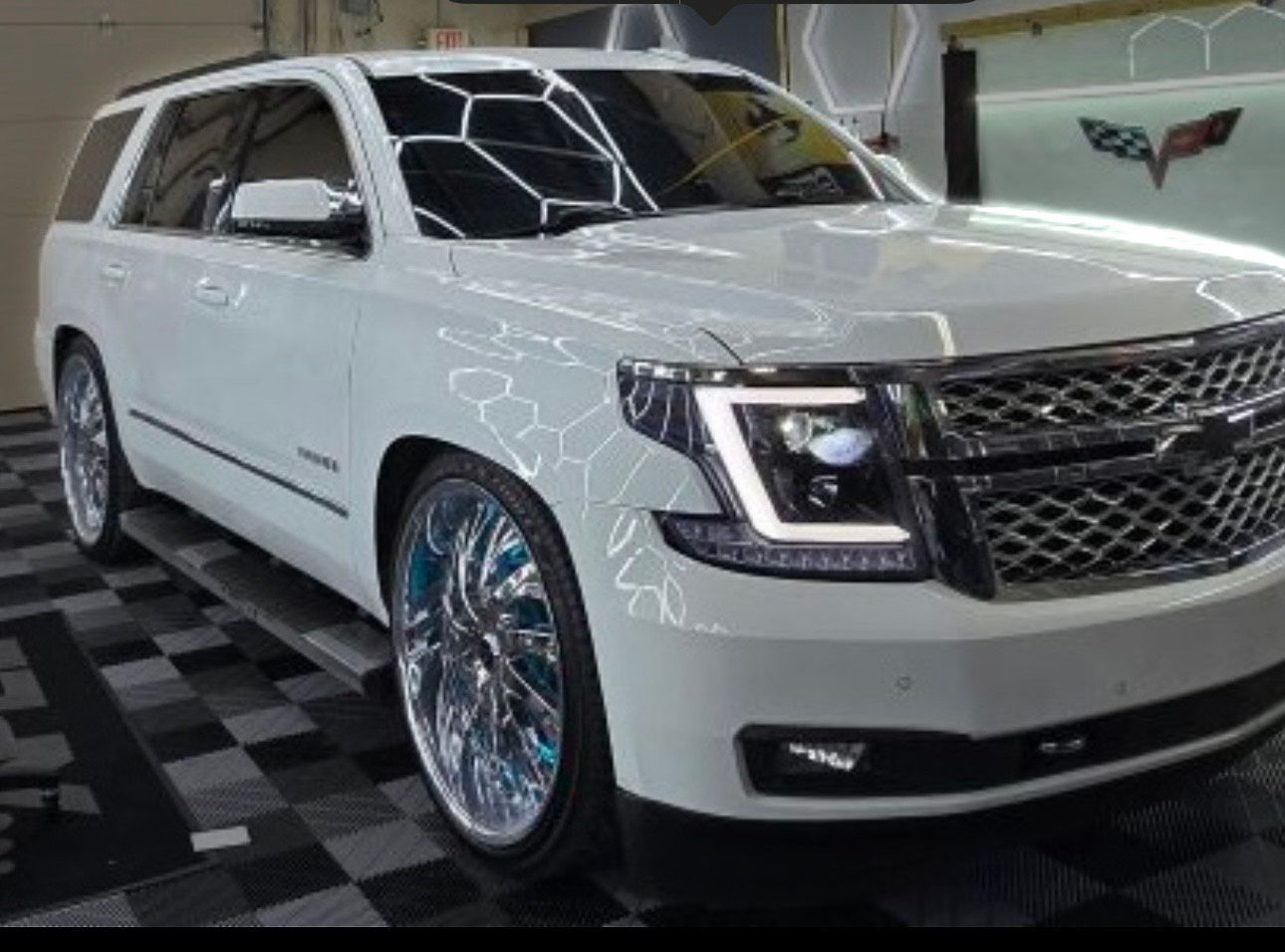 A white suv is parked on a checkered floor in a garage.