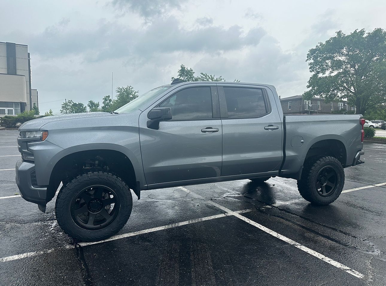 A silver truck is parked in a parking lot on a rainy day.