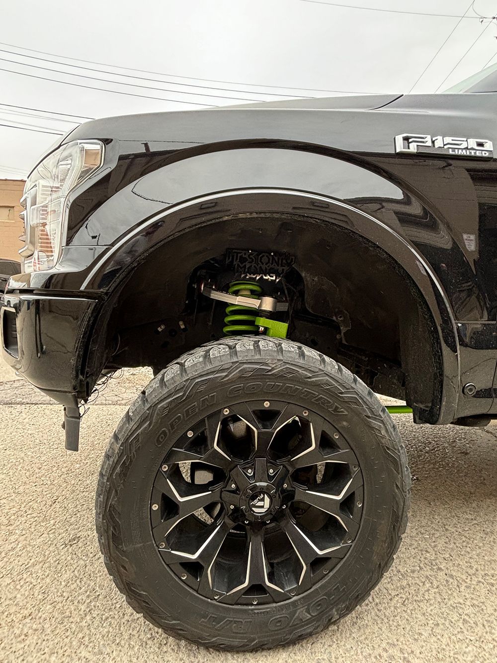 A black truck with black wheels and tires is parked on a gravel road.