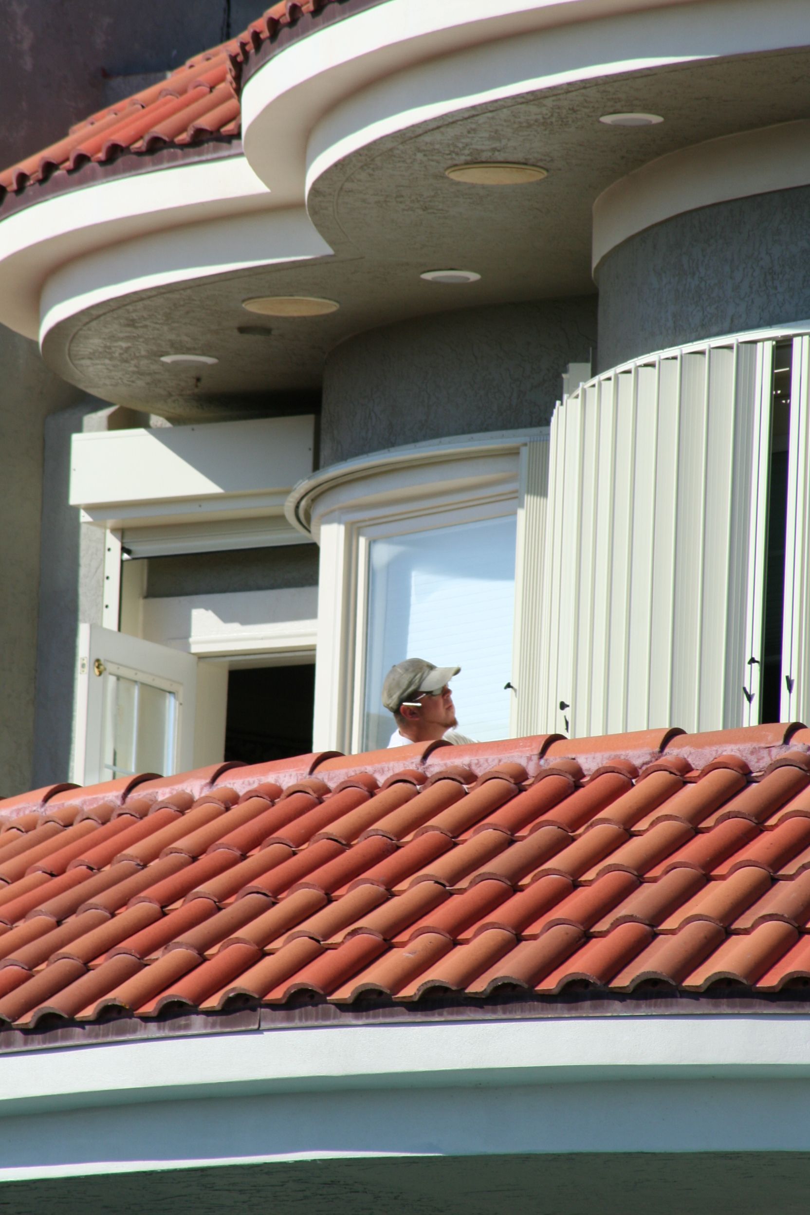 A man standing on a balcony with a red tile roof