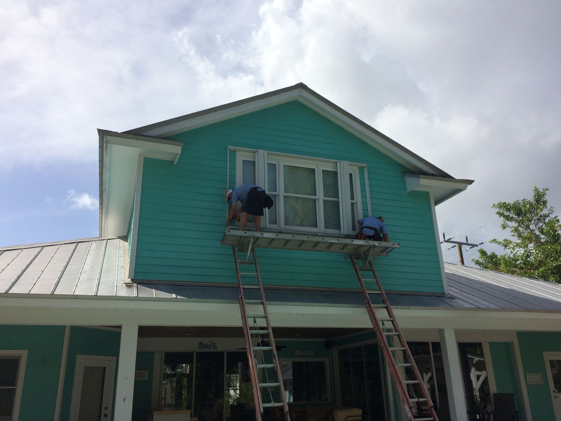 Two men are painting a blue house with ladders.