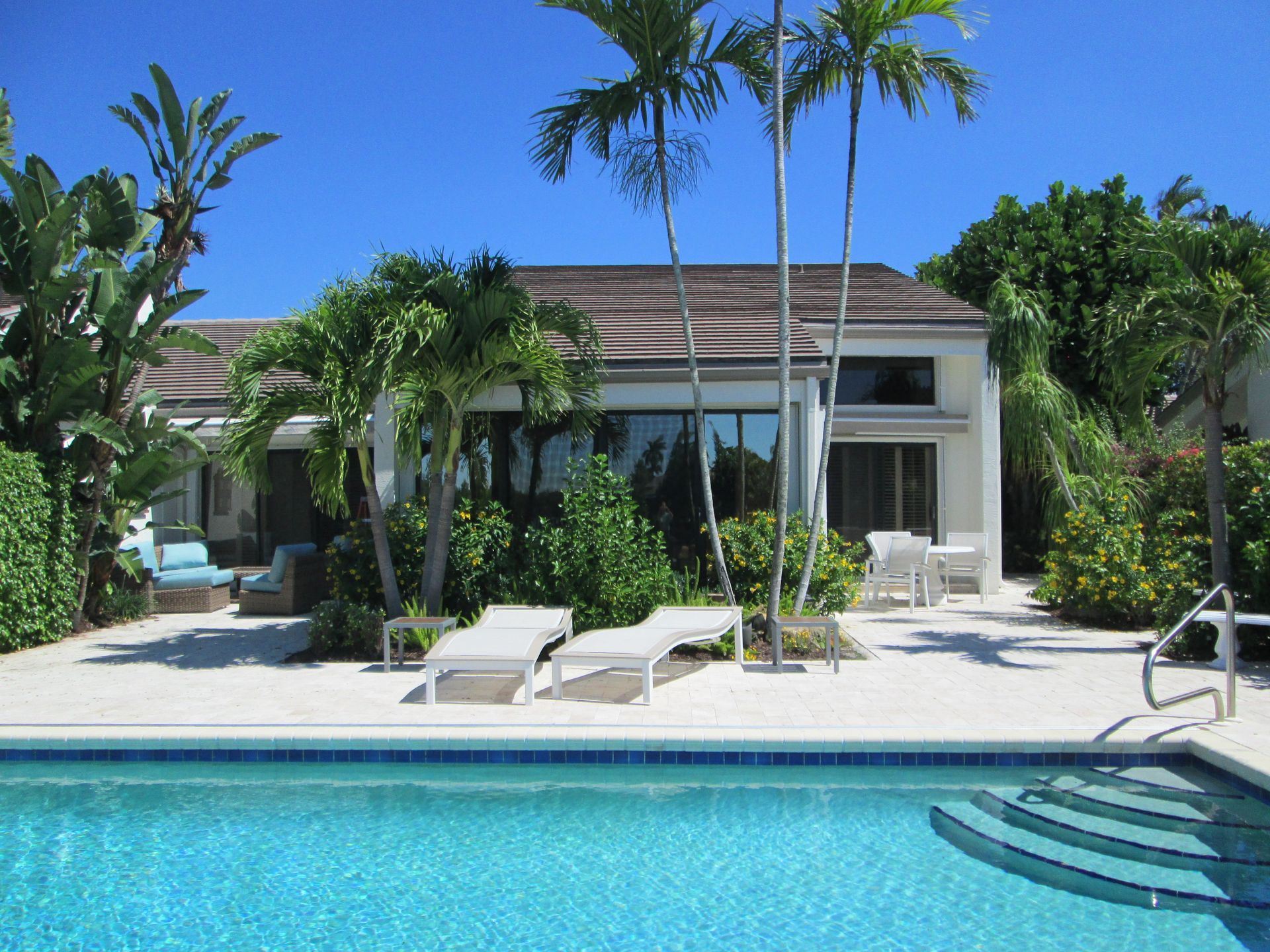 A swimming pool in front of a house with palm trees