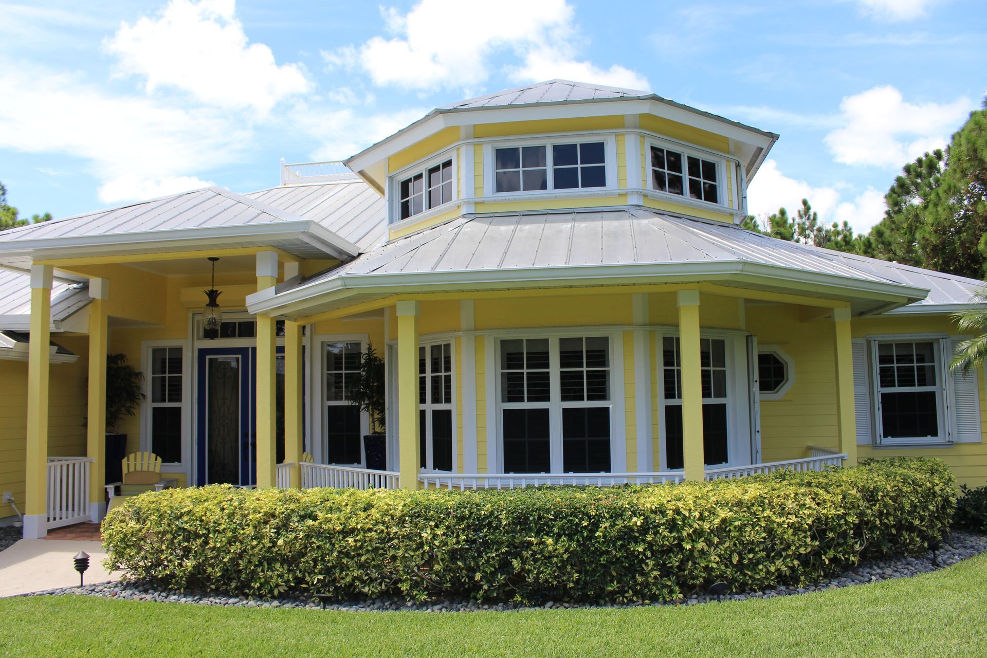 A yellow house with a silver roof and lots of windows