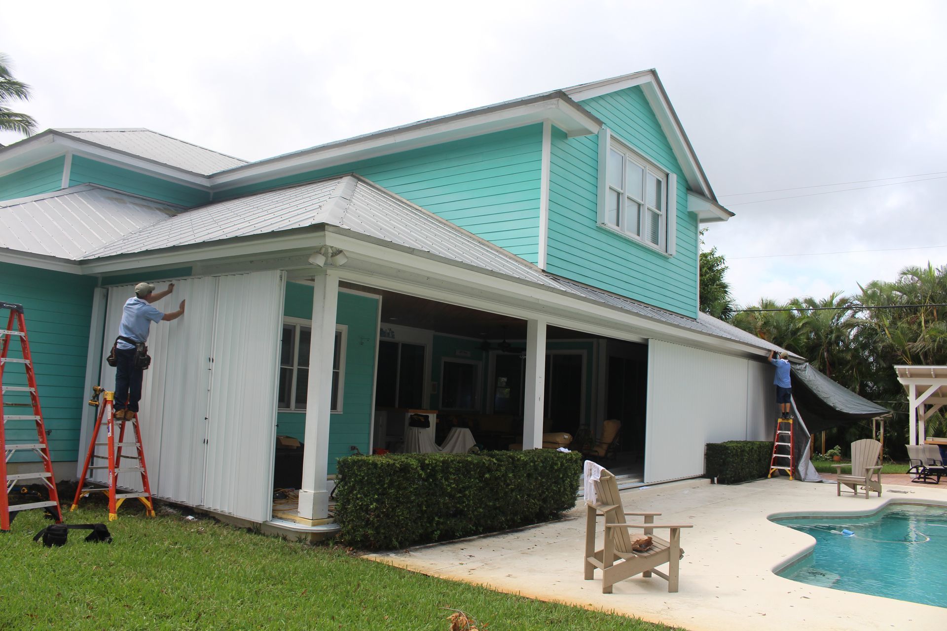 A man is painting the side of a house next to a pool.