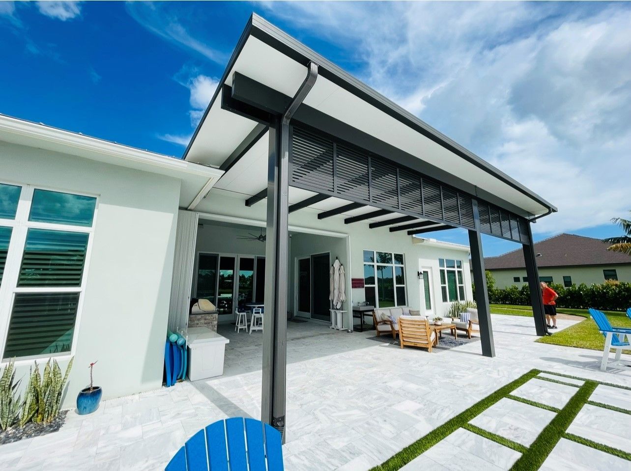 A patio with a pergola and chairs in front of a house.