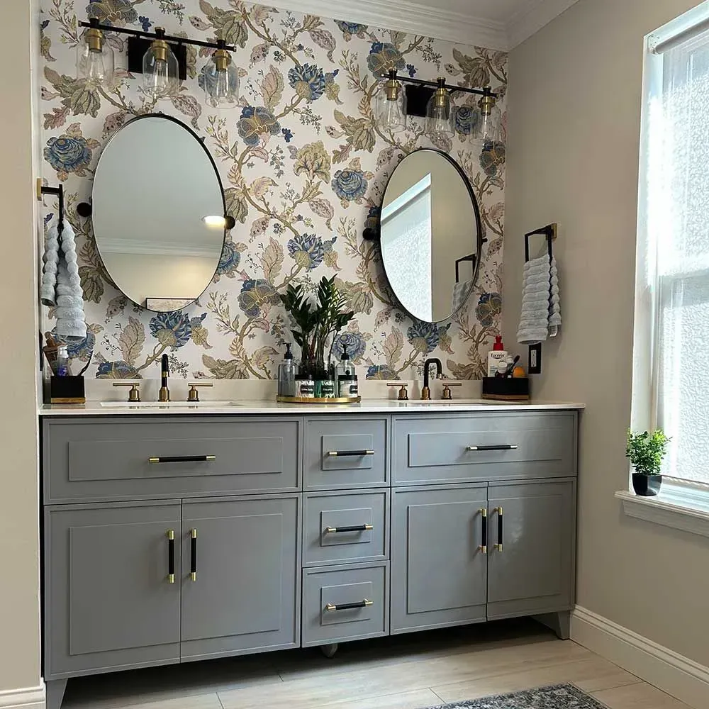 Double gray vanity with two oval mirrors and floral wallpaper in a modern bathroom.