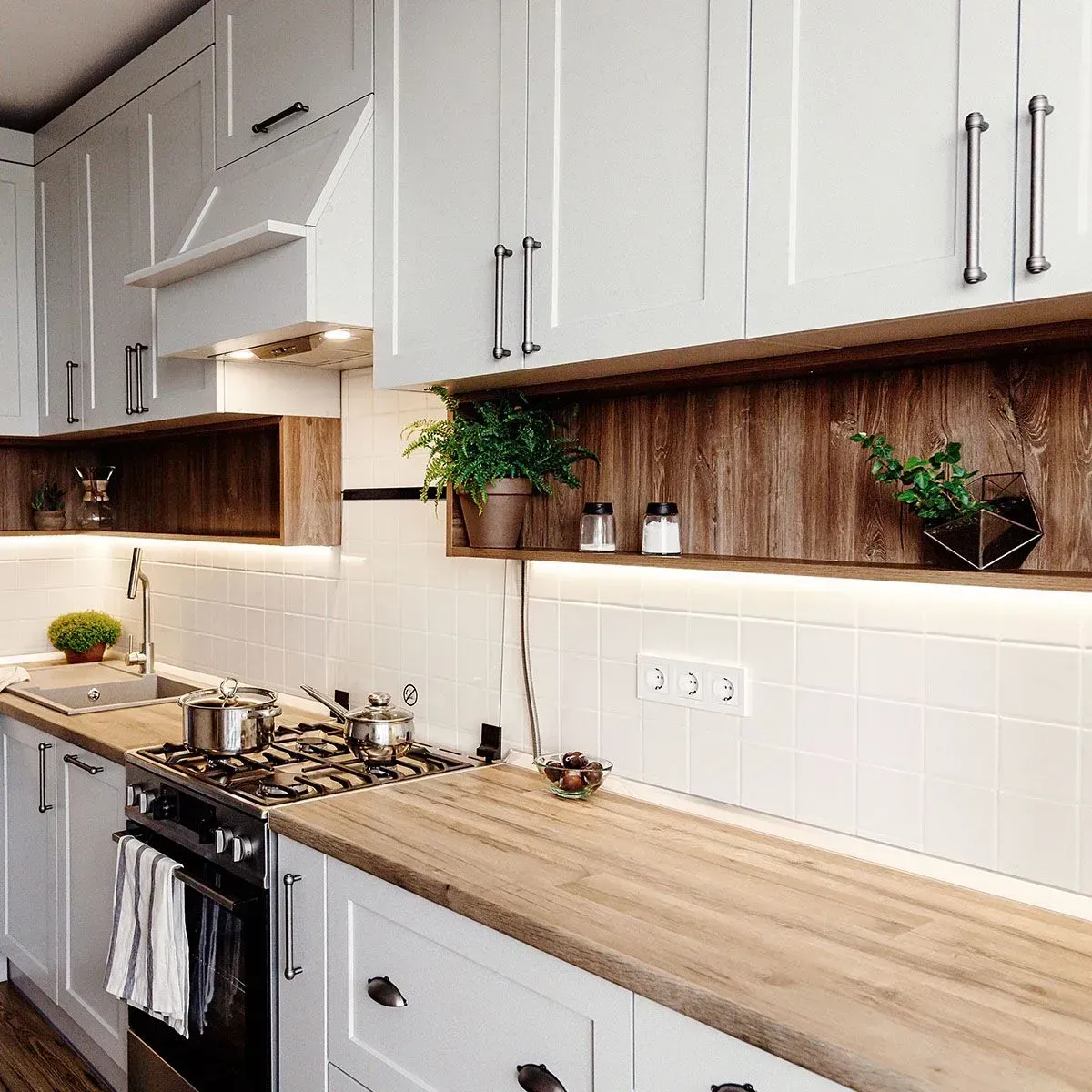 A modern kitchen featuring white cabinets, wood countertops, a tiled backsplash, and an open shelf with small plants.