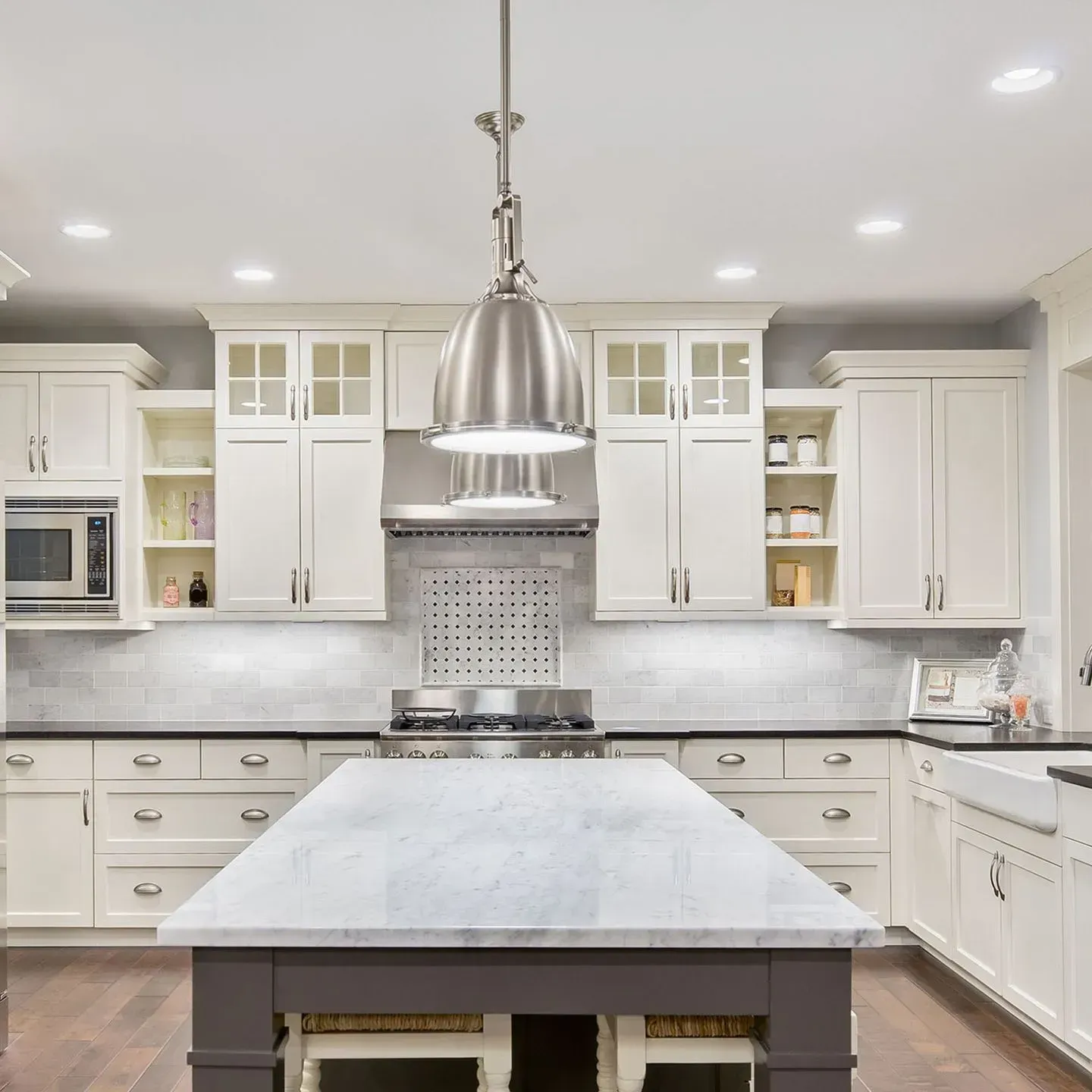A bright, modern kitchen featuring white cabinets, a central island with a dark base, and a large metal pendant light.