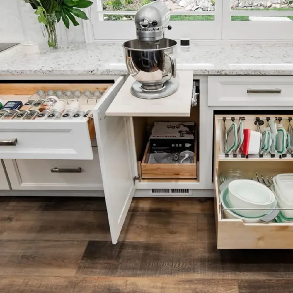 A kitchen cabinet with an open spice drawer, a pop-up mixer stand, and a pull-out shelf organized with bowls and lids.