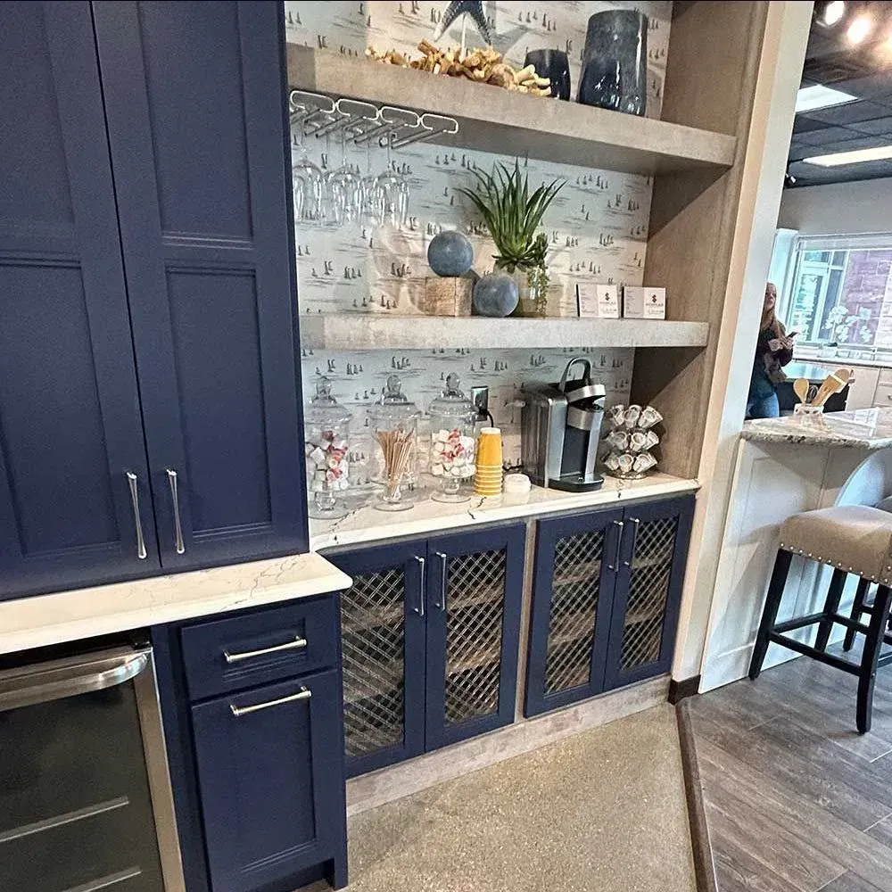 A navy blue kitchen coffee bar with open shelves, a patterned backsplash, and lower cabinets with metal mesh inserts.