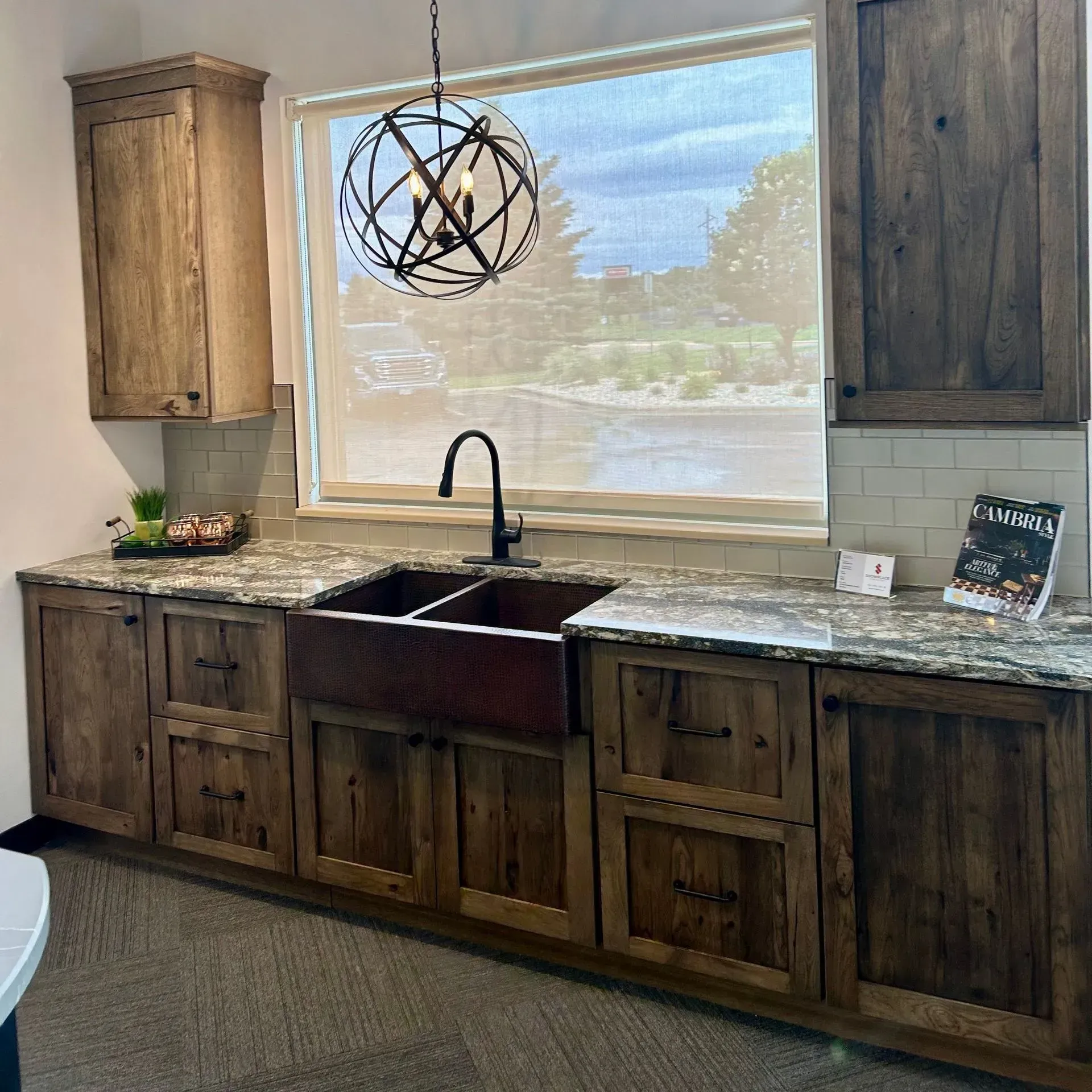 A rustic kitchen display featuring dark wood cabinets, a copper apron sink, granite countertops, and an orb chandelier.
