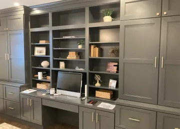 A dark gray home office built-in wall unit featuring open shelving, cabinetry, drawers, and a desk with a computer.