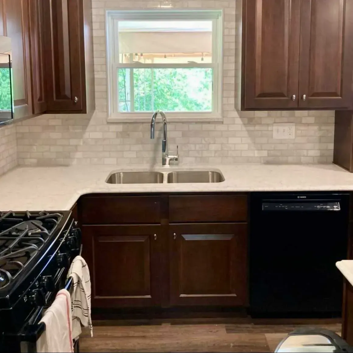 A kitchen view featuring dark wood cabinets, a light stone countertop, a double sink with a faucet, and a subway tile backsplash.