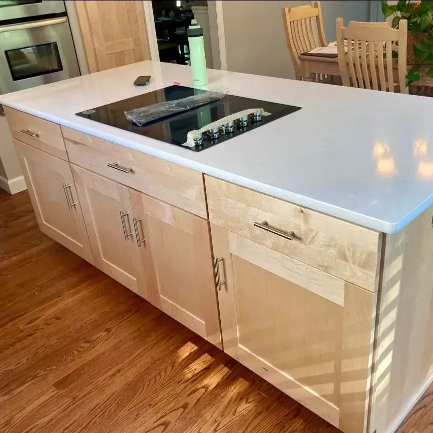 A light-wood kitchen island with a white countertop and a black electric cooktop on a hardwood floor.