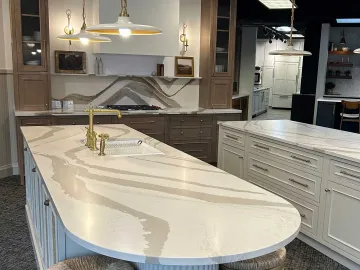 A kitchen showroom display featuring a large marble-topped island, wooden cabinetry, and modern pendant lighting.