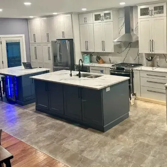 A modern kitchen featuring white cabinets, a large dark blue island with marble countertops, and stainless appliances.