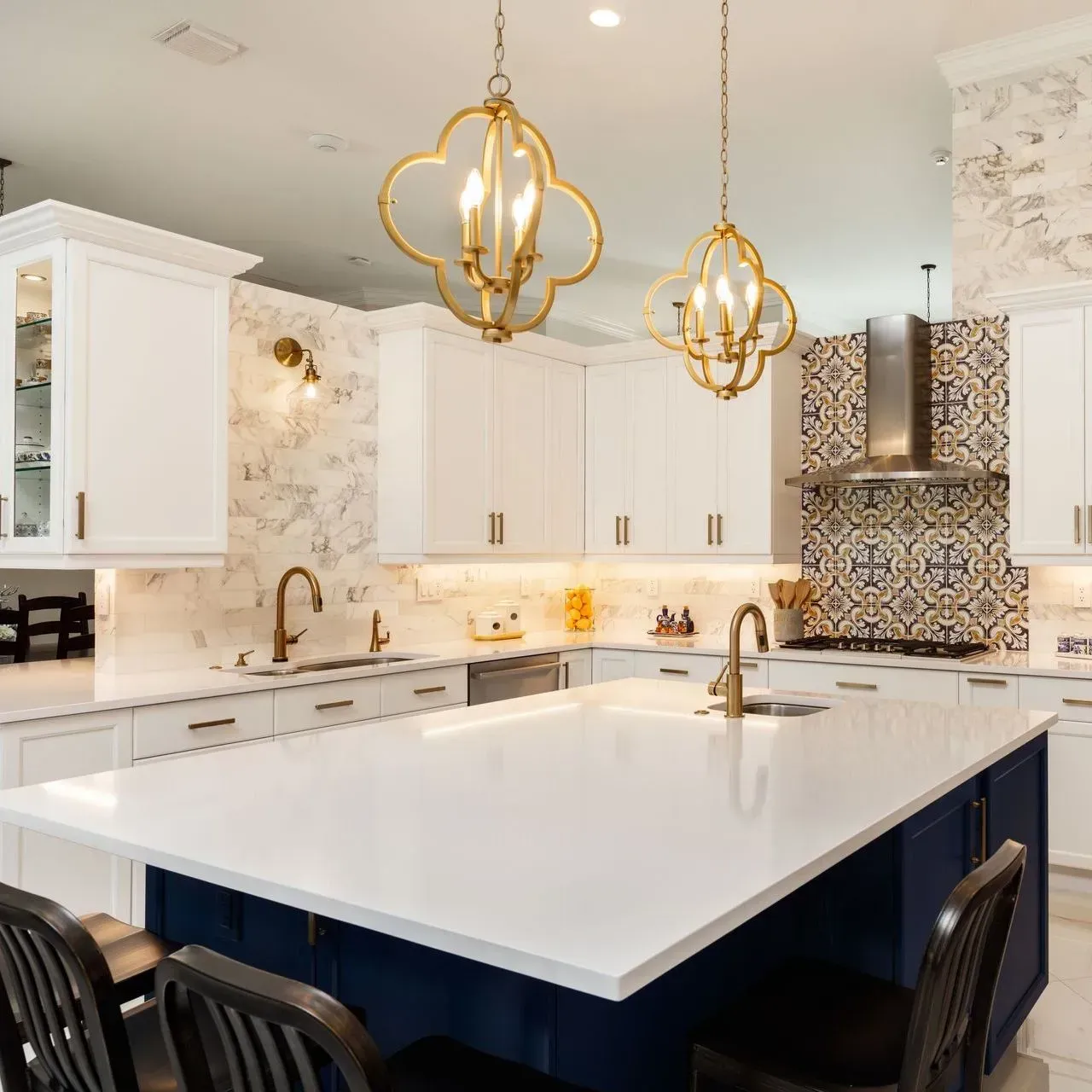 A modern white kitchen featuring a navy blue island with a quartz countertop, gold pendant lights, and patterned tile.