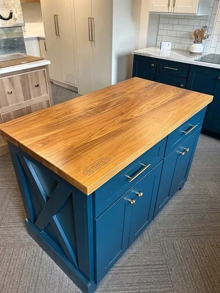 A blue kitchen island with a natural wood countertop, featuring X-pattern side detailing, set in a bright kitchen.