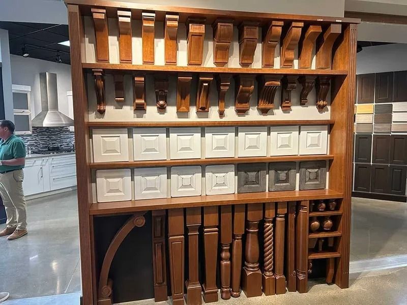 A display shelf in a showroom featuring various wooden corbels, cabinet door samples, and architectural furniture legs.