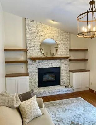 A cozy living room with a white-washed brick fireplace, built-in wooden shelves, a mirror, and a beige sofa.