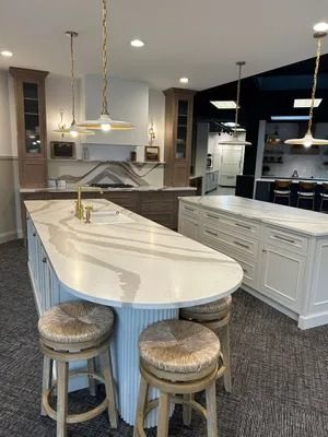 Two kitchen islands with white marble-style countertops, one rounded with wooden stools, inside a bright showroom.