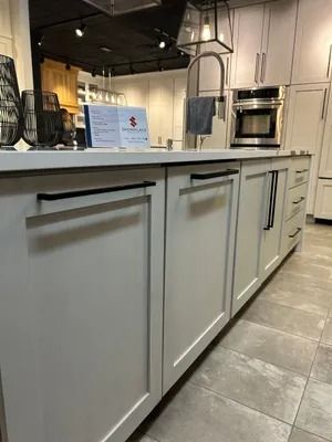 A low-angle view of a modern kitchen island with light gray shaker cabinets, matte black handles, and tile flooring.
