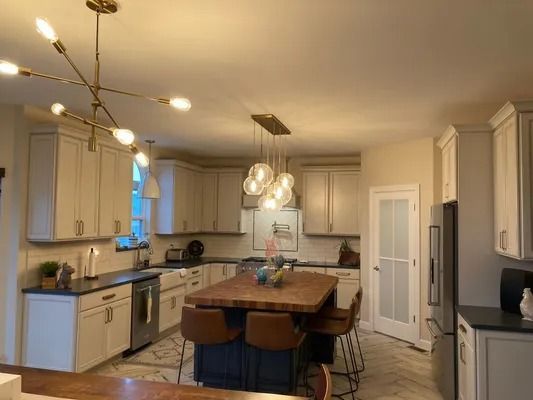 Modern kitchen with white cabinets, dark countertops, a dark blue island with bar stools, and two stylish light fixtures.