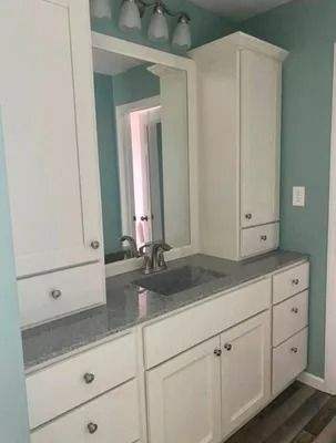A bathroom vanity with white cabinets, gray granite countertops, and light blue walls, featuring a mirror and sink.