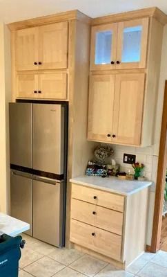 A stainless steel refrigerator next to light-wood cabinets with a matching set of drawers and a countertop.