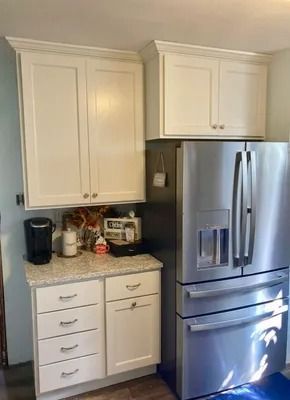 Off-white kitchen cabinets and drawers next to a stainless steel refrigerator with a countertop coffee station.