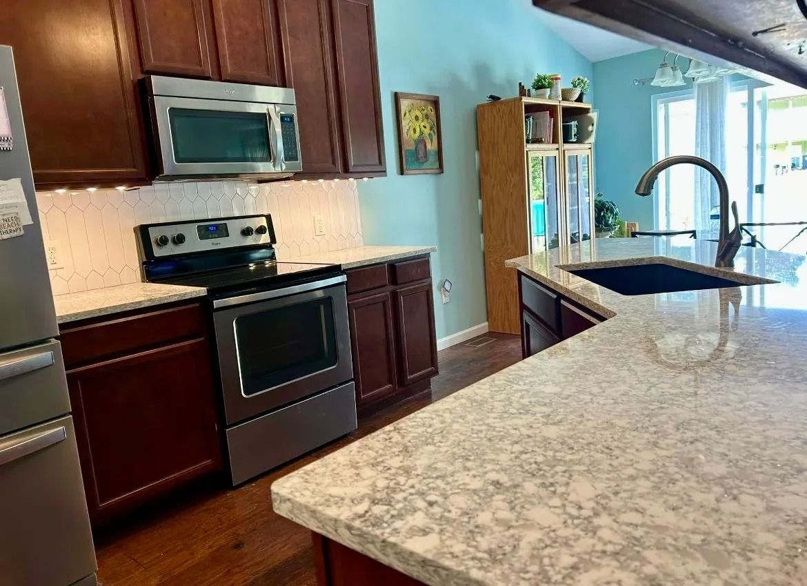 A modern kitchen with dark wood cabinets, stainless steel appliances, a light-colored granite countertop, and blue walls.