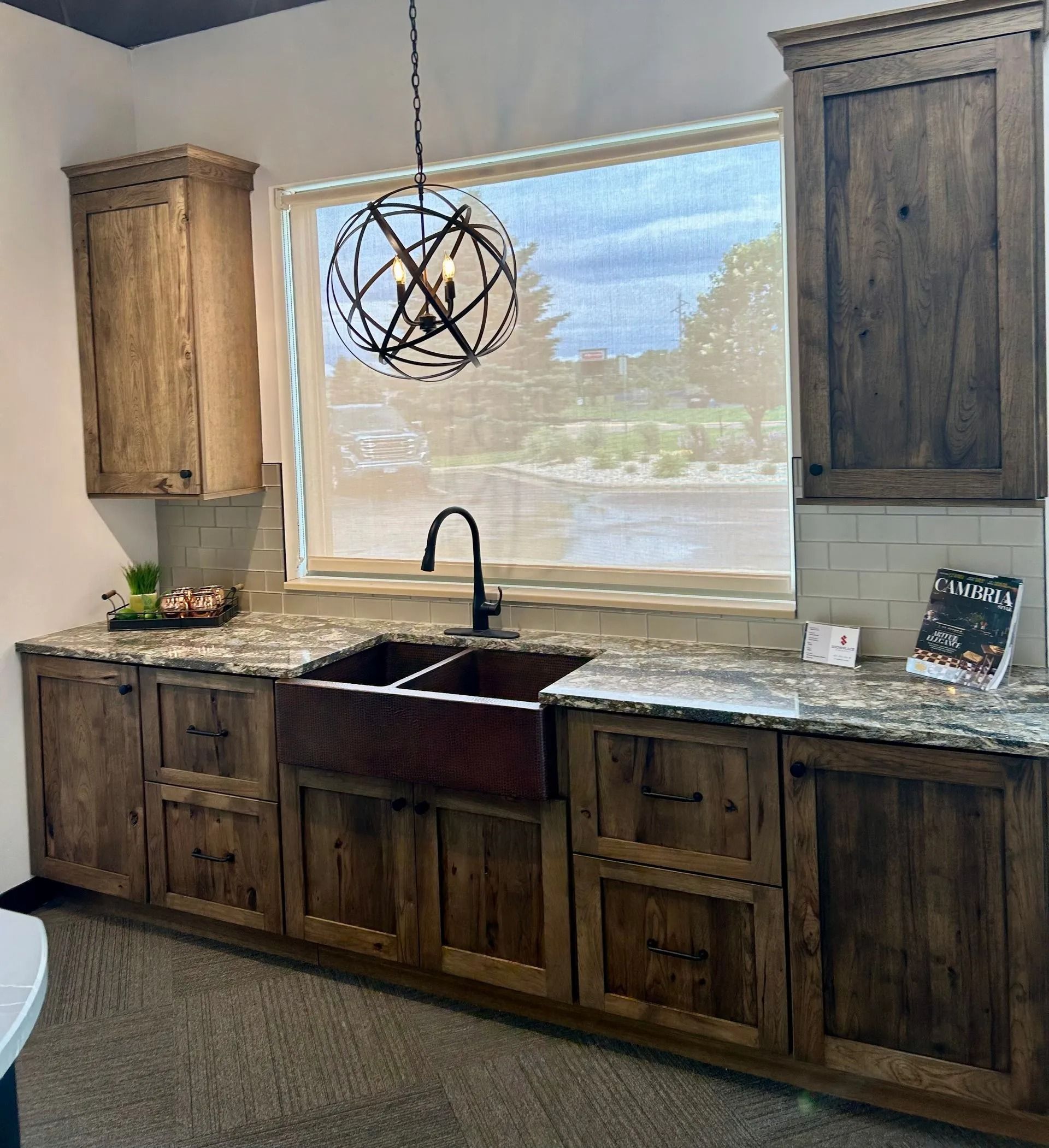 Rustic kitchen featuring brown wooden cabinets, a farmhouse sink, granite countertops, and a spherical pendant light.