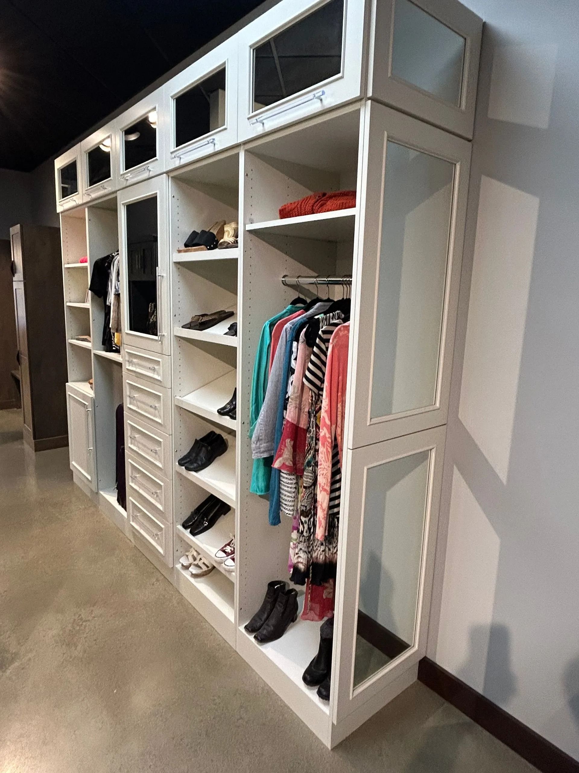 A white, multi-section wardrobe organizer unit with shelves, hanging space for clothes, and mirrored cabinet doors.