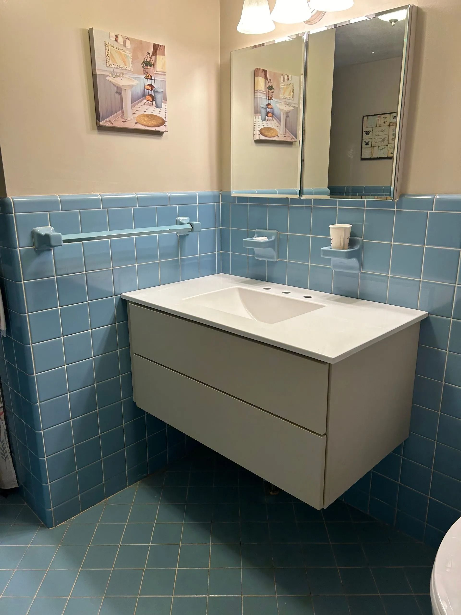 A wall-mounted bathroom vanity with a white sink against blue tiled walls and a medicine cabinet mirror above.