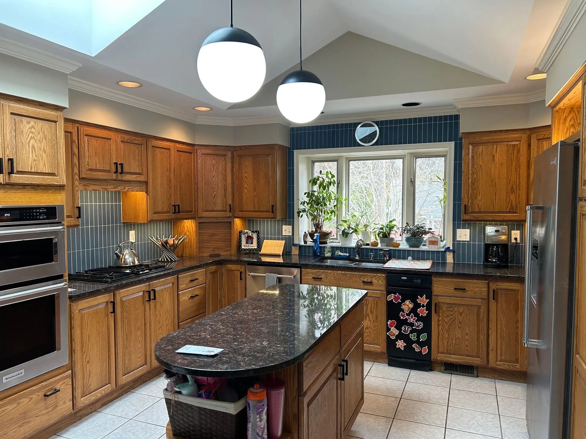 A kitchen with oak cabinets, a dark granite island, stainless steel appliances, and two hanging globe pendant lights.