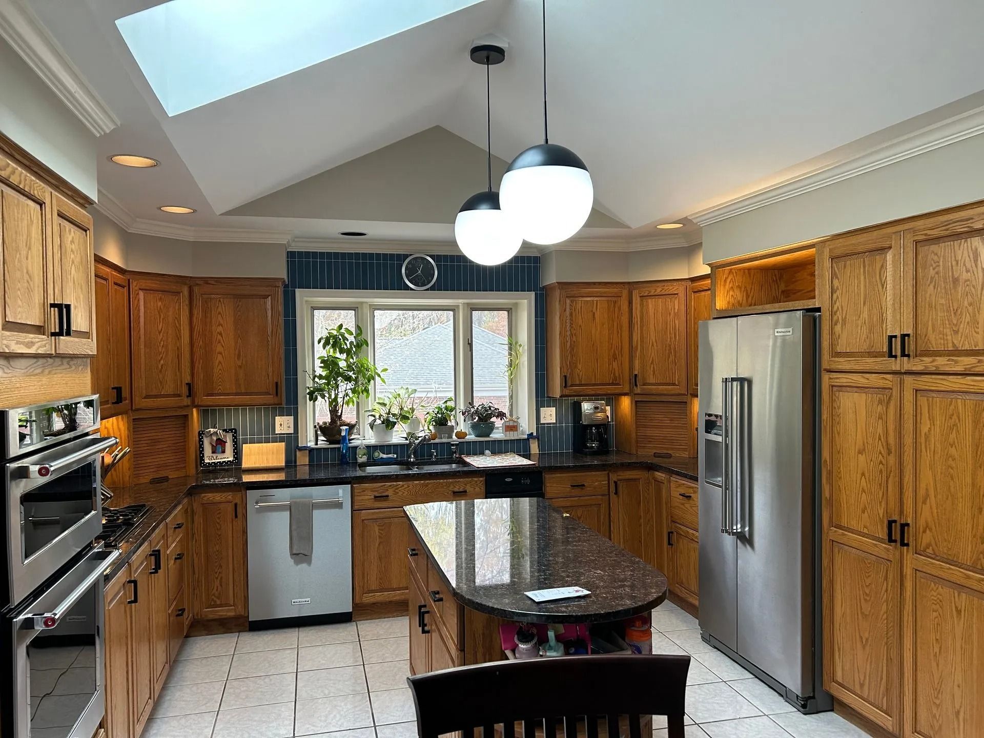 A wood-cabinet kitchen with a central island, dark granite countertops, stainless appliances, and skylights.