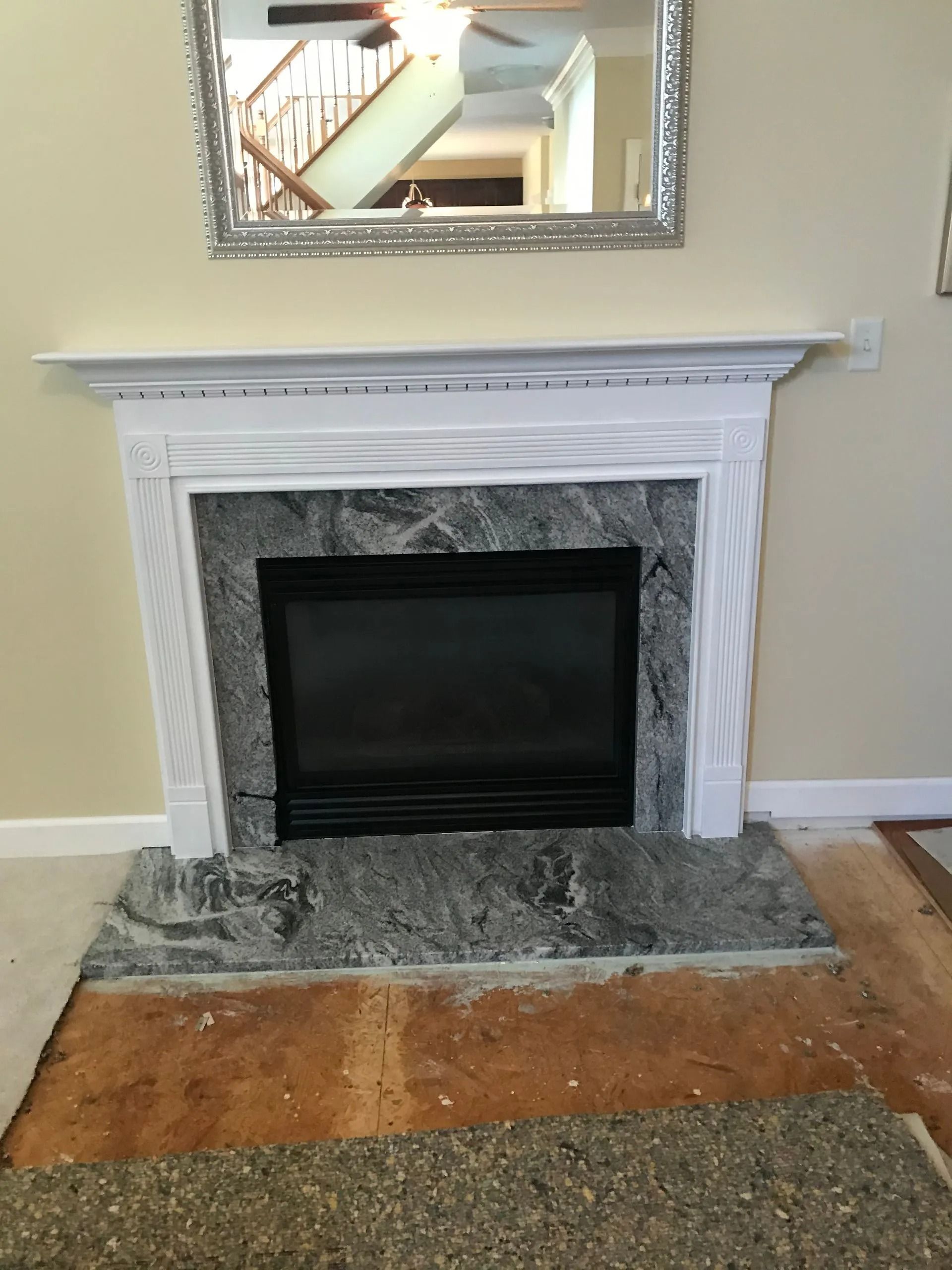 A fireplace with a white mantel and a gray, mottled stone surround and hearth, featuring a mirror hanging above it.
