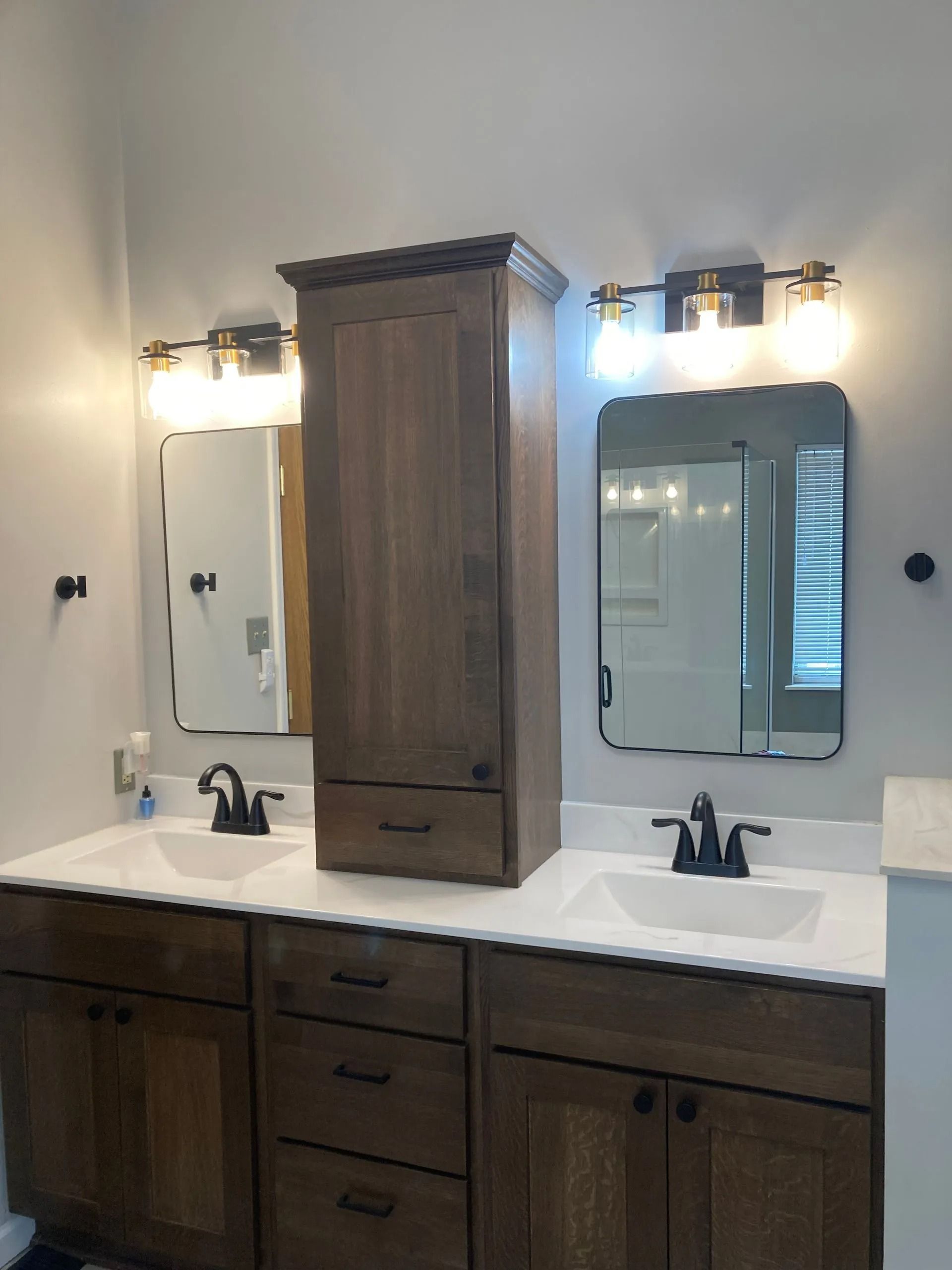 Double bathroom vanity with a central wooden cabinet, two sinks, mirrors, and vintage-style light fixtures.