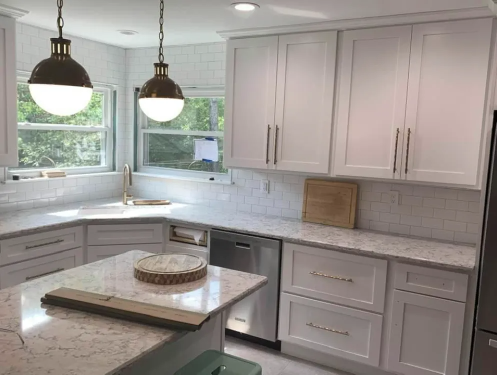 A modern kitchen featuring white cabinets, light quartz countertops, subway tile backsplash, and two pendant lights.
