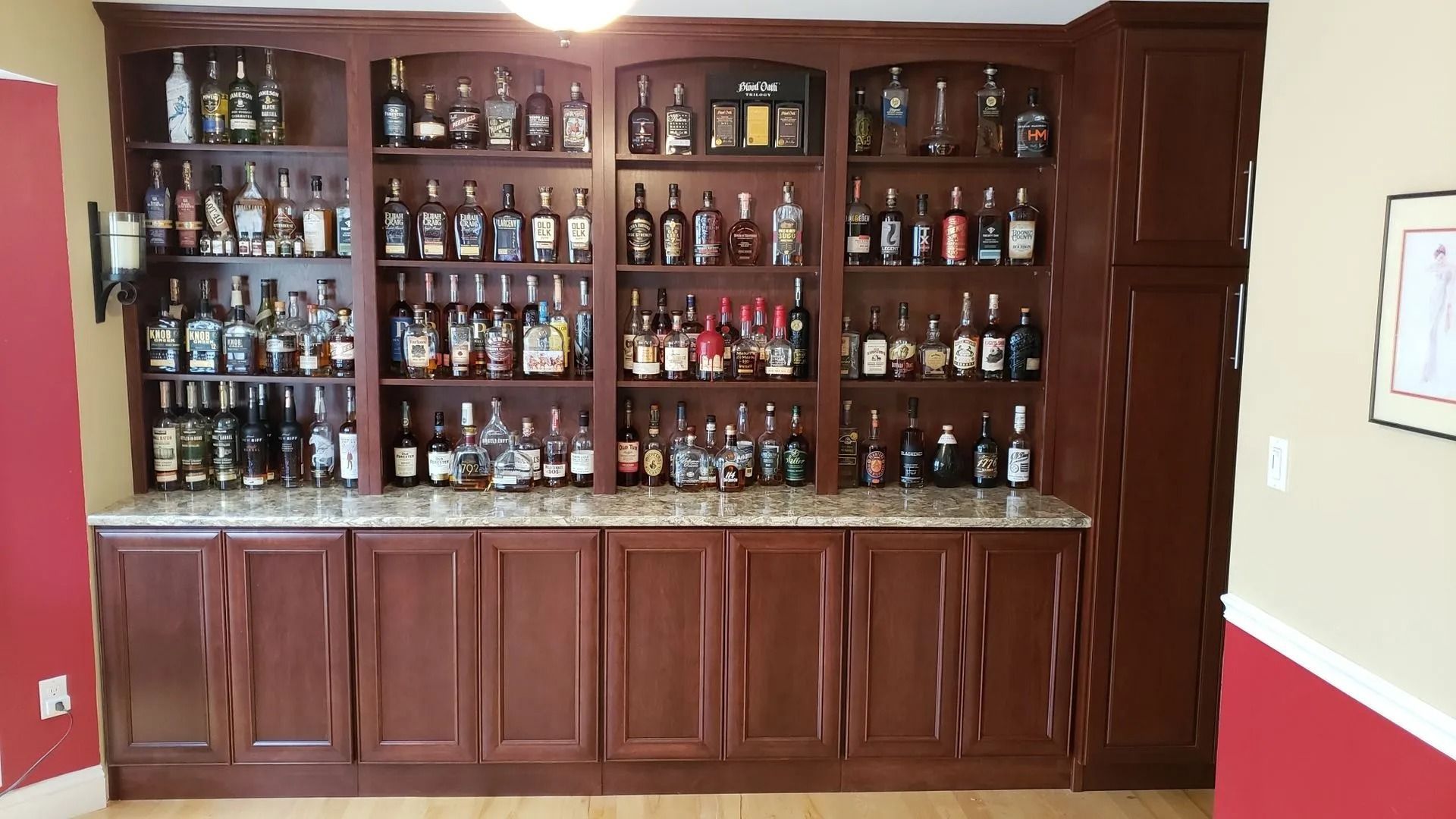 A large, dark wood built-in bar with granite countertops and open shelving stocked with various liquor bottles.