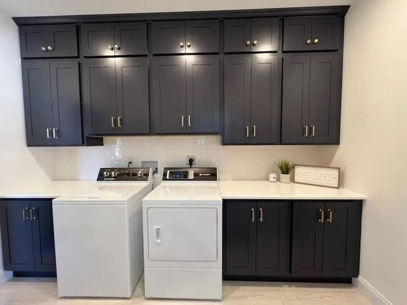 A modern laundry room with white washer and dryer, dark charcoal cabinets, and white countertops.