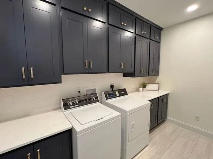 A laundry room with dark blue cabinets, white countertops, and white washer and dryer units against light walls.