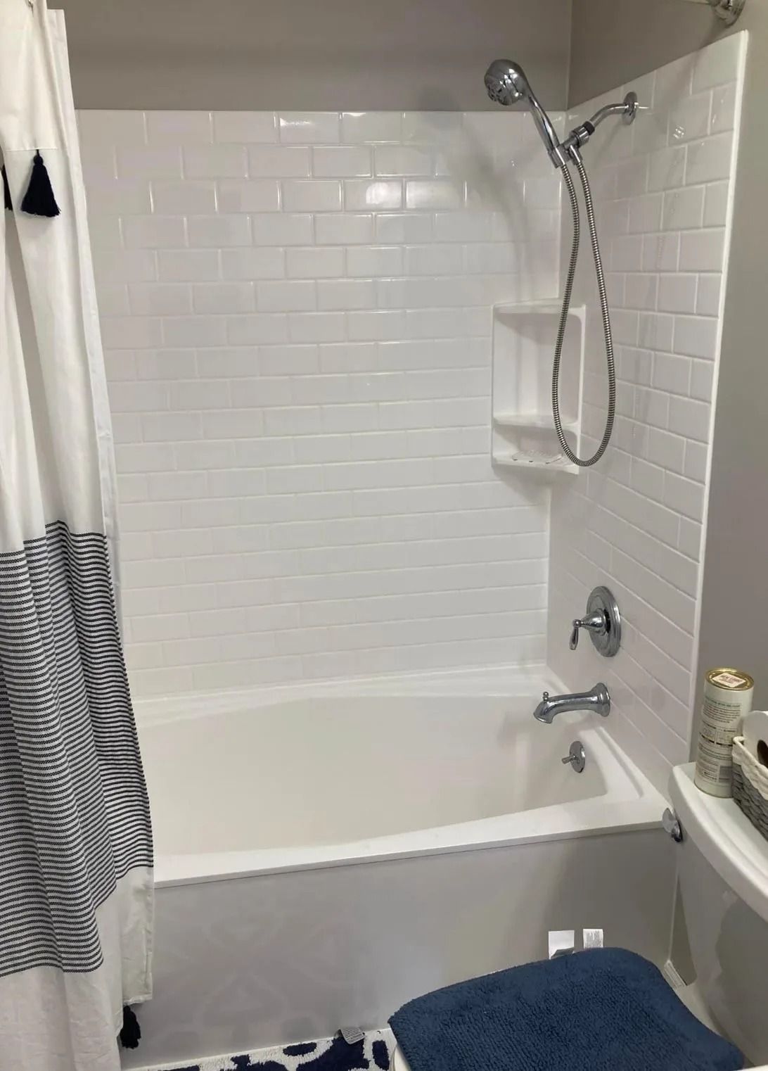 A bathroom shower and tub combination featuring white subway tile walls, a handheld showerhead, and a curtain.