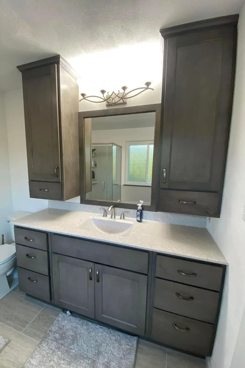 A dark-wood vanity with light countertops and two side towers flanking a mirror in a bathroom.