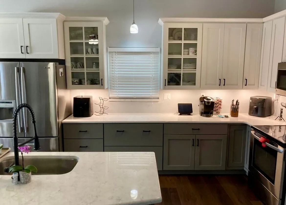 A two-tone modern kitchen with white upper cabinets, gray lower cabinets, a marble countertop, and stainless appliances.