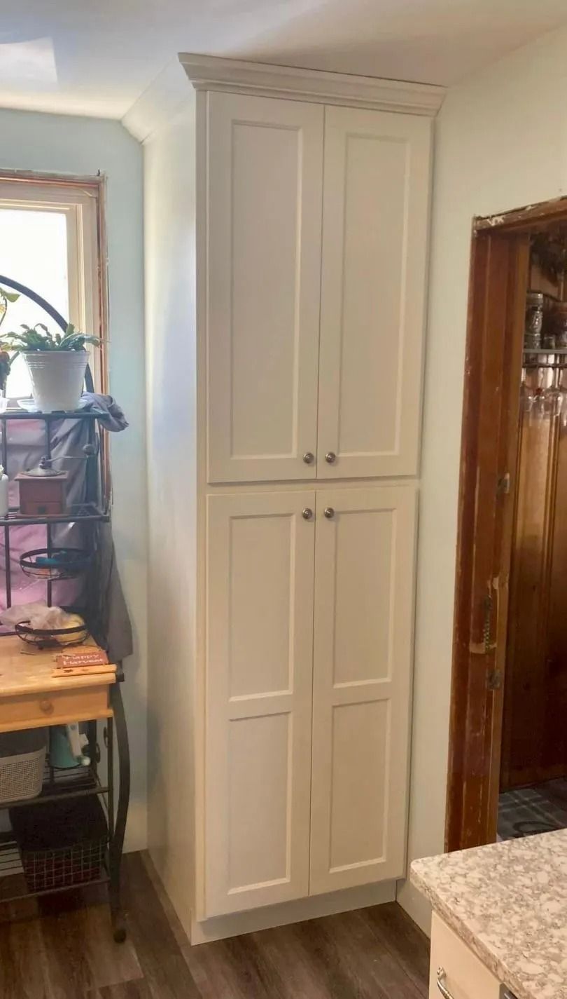 A white, floor-to-ceiling cabinet with four doors stands in the corner of a room next to a wooden door frame.
