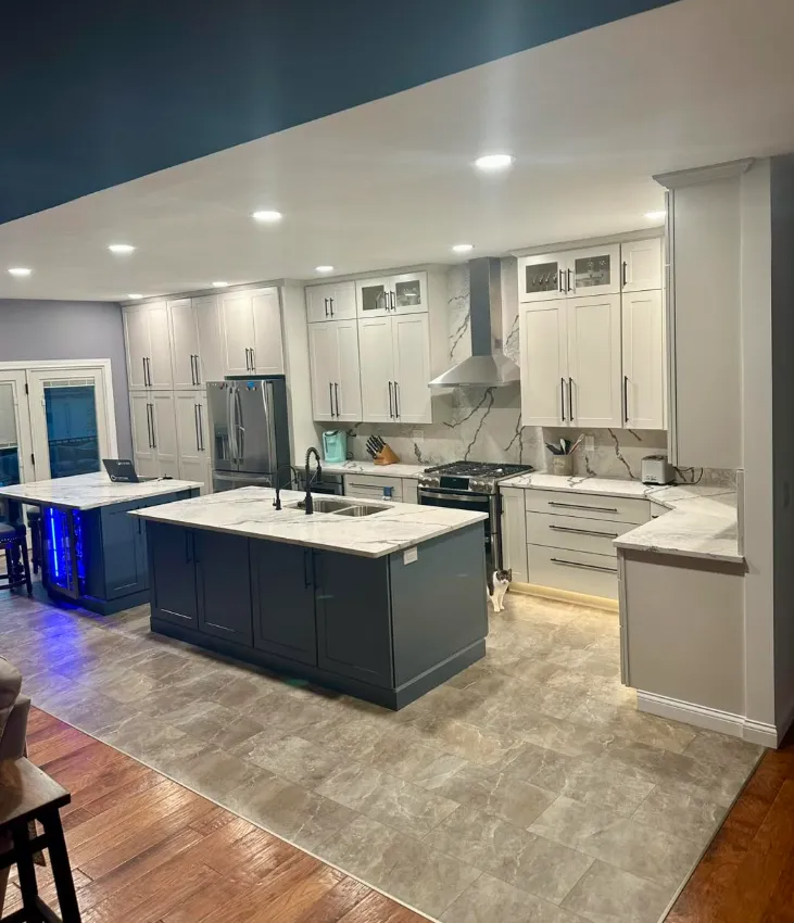 A modern kitchen with two islands, grey cabinetry, white marble-patterned countertops, and tile flooring.