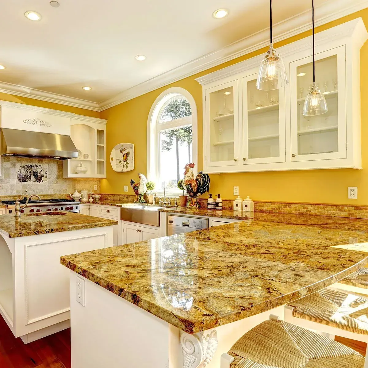 A sunny yellow kitchen with white cabinetry, granite countertops, an island with bar stools, and two pendant lights.